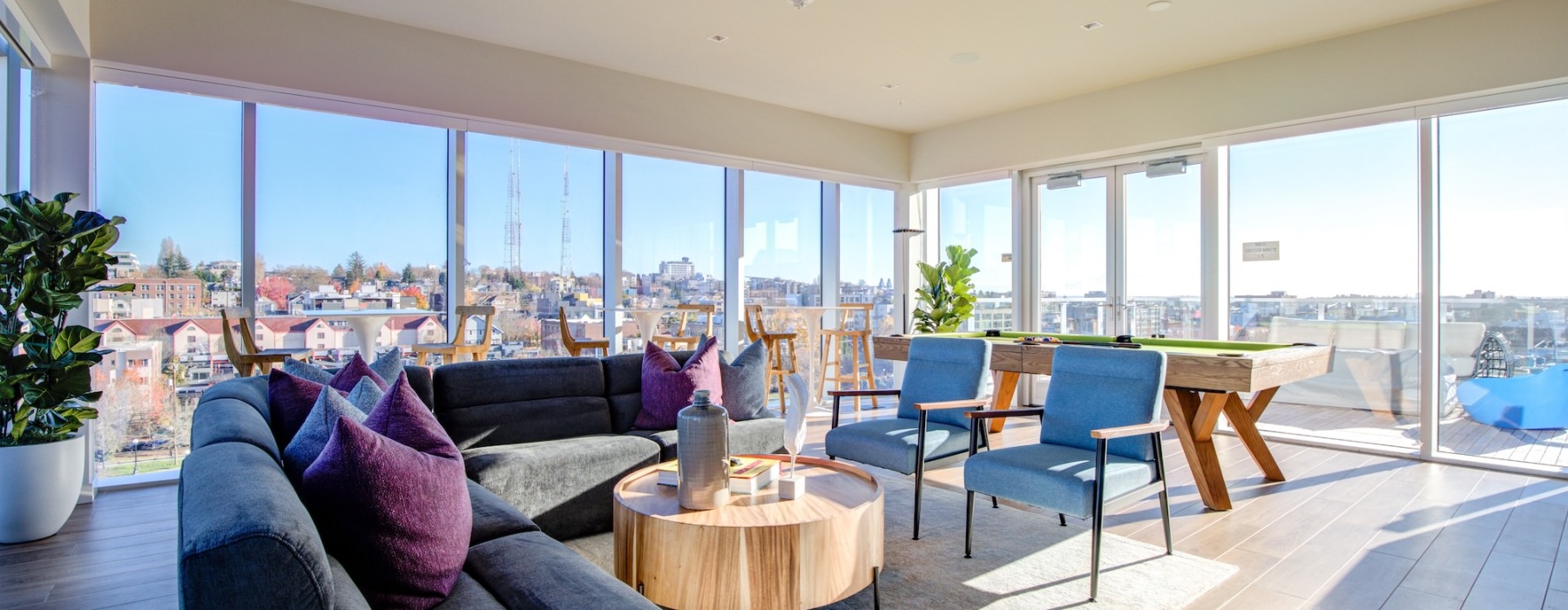Sky lounge with large windows, couches and a pool table at Connection on Broadway luxury apartments in Capitol Hill, Seattle.